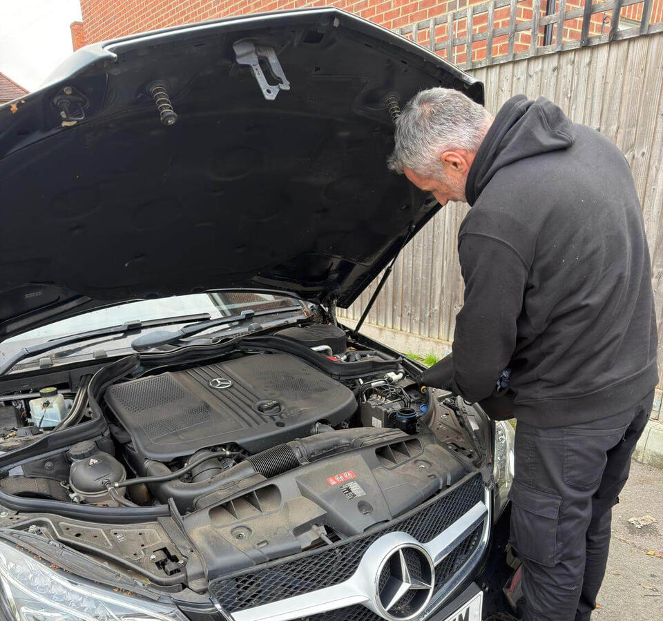 Mobile mechanic carrying out a car service Graeme, a mobile mechanic from Maxamy, carrying out a car service on a Mercedes with the bonnet open at a customer’s home.