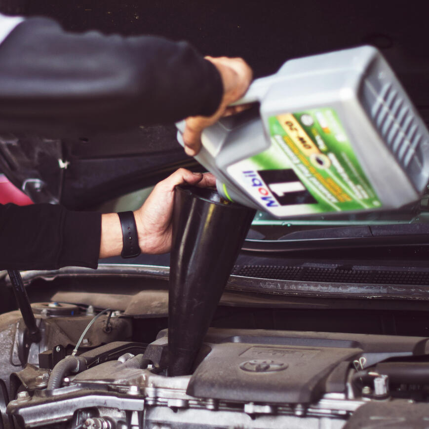Engine Oil Top‑Up During Mobile Service Close‑up of a mechanic pouring fresh engine oil into a car using a funnel, illustrating Maxamy’s mobile servicing and maintenance across Berkshire.