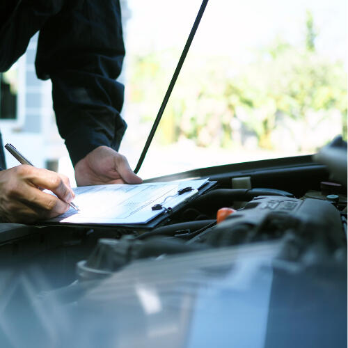 Mechanic Completing Vehicle Inspection Checklist A mechanic notes findings on a clipboard while inspecting a car’s engine bay, symbolising Maxamy’s thorough mobile diagnostics and vehicle inspections.