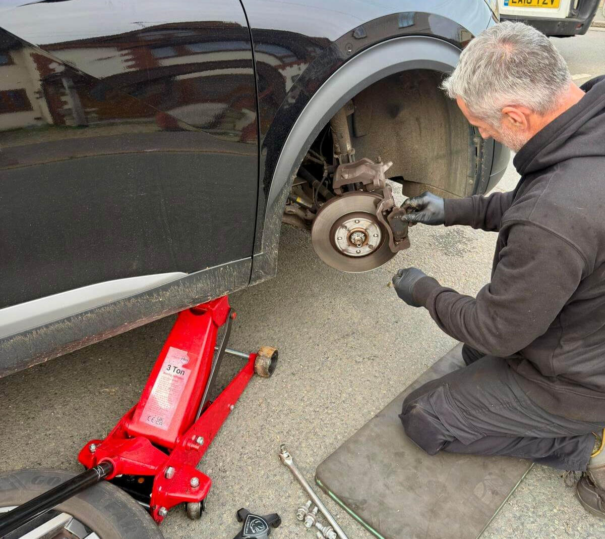 Mobile brake repair in Maidenhead Mechanic replacing front brake components on a black SUV with a mobile jack during a driveway repair in Maidenhead.