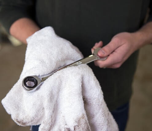 Mechanic cleaning tools after a mobile service – Maxamy Autocare Mechanic wiping down a ratchet tool with a cloth after completing a mobile car service, showcasing attention to detail and cleanliness.